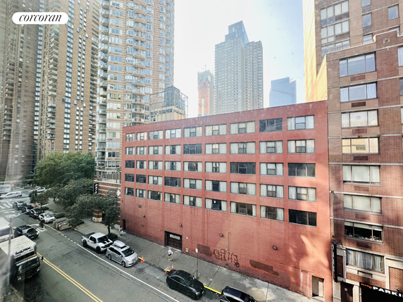 View of a red brick mid-rise building surrounded by taller skyscrapers.