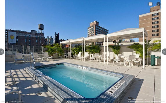 Rooftop view showing a swimming pool with sun loungers and canopies overlooking a cityscape.