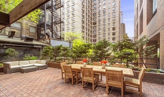 Outdoor patio area with seating and dining table adjacent to tall buildings.