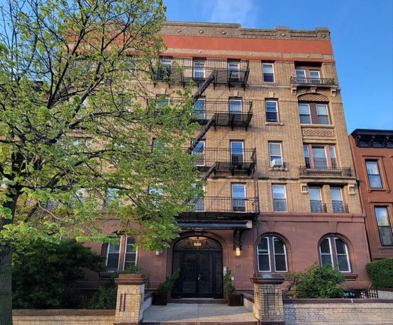 Front view of a multi-story brick apartment building with fire escapes.
