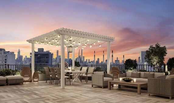 Rooftop with seating area and pergola adorned with string lights, overlooking city skyline at sunset.