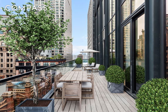 Rooftop terrace with outdoor furniture and potted plants, offering a view of surrounding high-rise buildings.