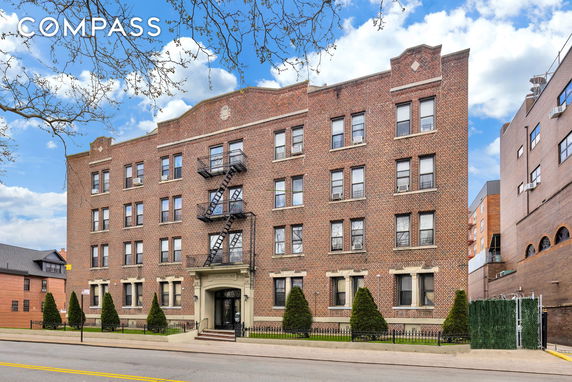Front view of a multi-story brick apartment building with a central entrance and fire escape.
