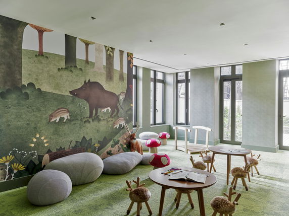 Indoor play area with animal-themed wall mural, small tables, and child-sized seating.