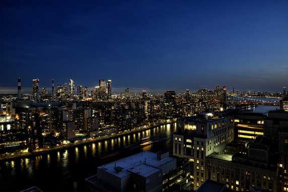 Panoramic view of a city skyline at night with illuminated buildings along a river.