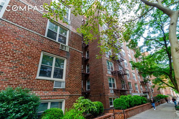 Front view of a multi-story brick apartment building with several windows and fire escape.