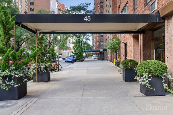 Front view of a building with a canopy and plants along the entrance walkway.