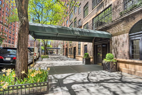 Front view of a multi-story brick building with green awnings and potted plants near the entrance.