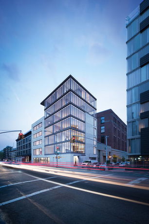 Front view of a modern multi-story glass and concrete building located at a street corner.