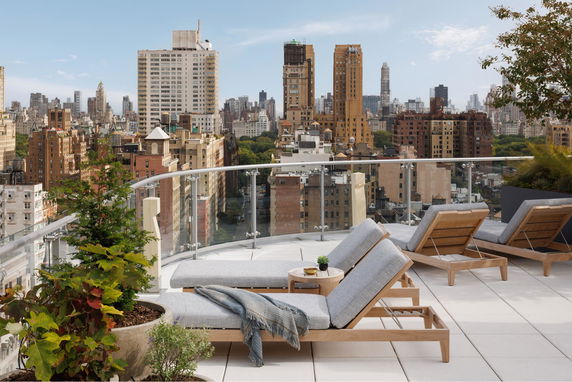 Rooftop terrace with lounge chairs and potted plants, overlooking a city's skyline.