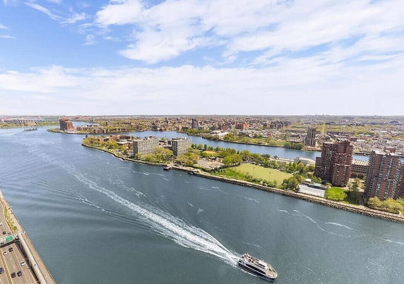 Panoramic view of a river with buildings and green areas along the shoreline.