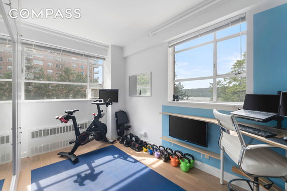 Room with exercise equipment and a desk with a computer setup by large windows.