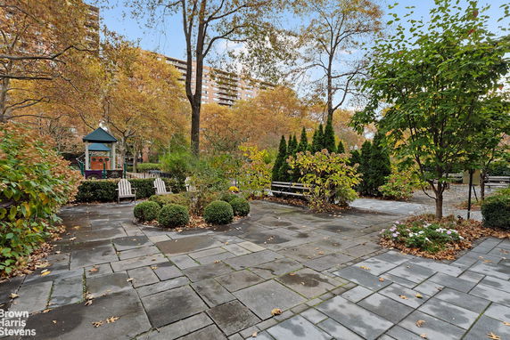 Outdoor play area with a small playground structure, benches, and surrounding trees.