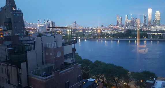 Panoramic view of a city skyline and river with a bridge at dusk.