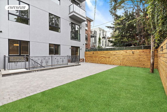 View of the back of a multi-story building with a fenced patio and grass area.