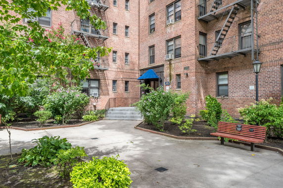 Front view of a brick apartment building with fire escapes and a blue canopy entrance.