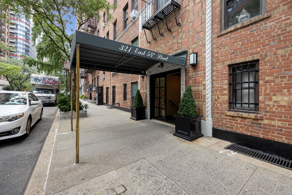 Front view of a brick building with a canopied entrance and potted plants.