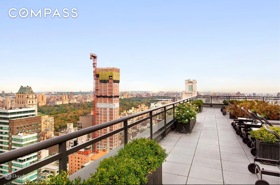 Rooftop terrace with plants and lounge chairs overlooking cityscape.