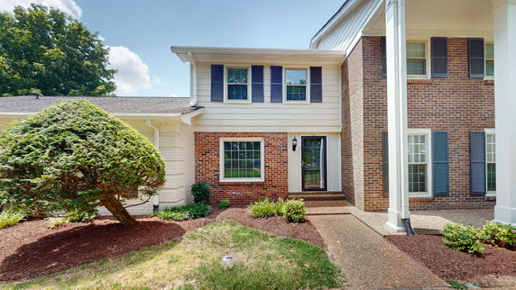 Front view of a two-story brick house with a prominent entrance and windows with shutters.