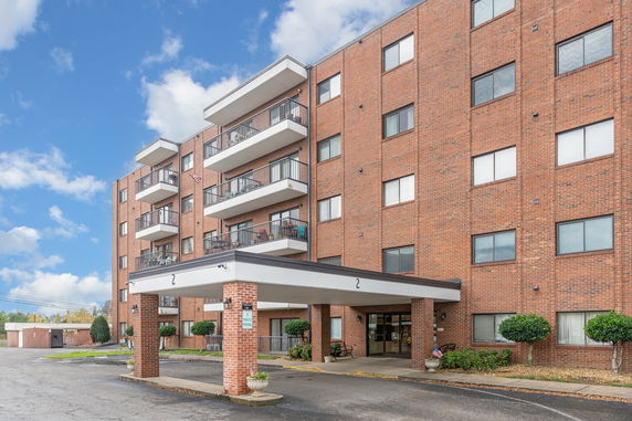 Front view of a multi-story brick apartment building with balconies and a covered entrance.
