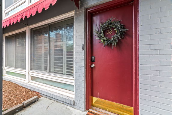 Front view of a building entrance with a red door and large windows, featuring a decorative wreath on the door.