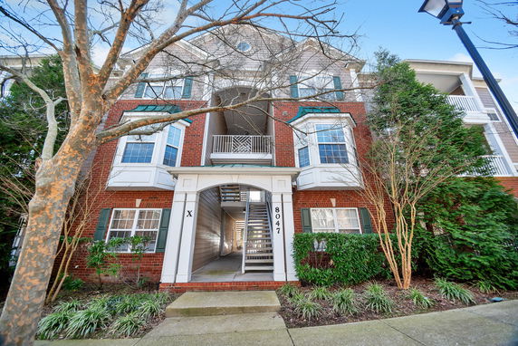 Front view of a multi-story building with brick and white siding, featuring balconies and a central staircase.