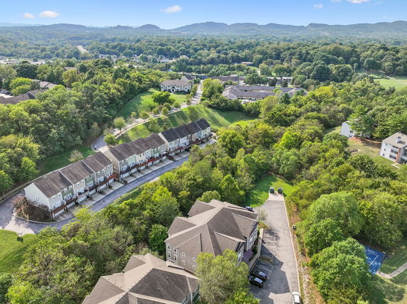 Wide aerial view of a residential area surrounded by greenery and hills.