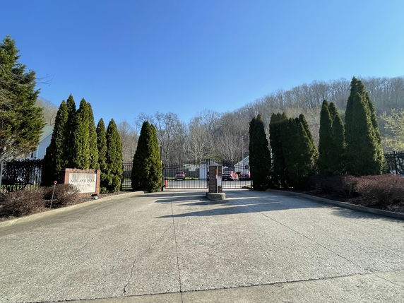Front view of a gated community entrance with a driveway and trees.