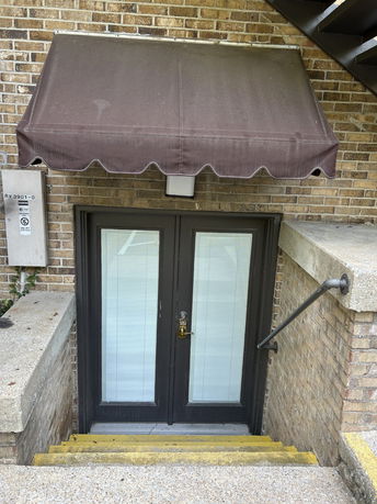 Exterior view of a building entrance with a covered door and steps leading down.