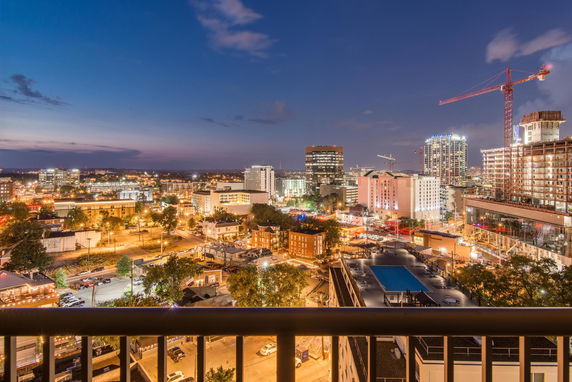 Wide view of a cityscape at night with buildings, cranes, and a swimming pool visible from a high vantage point.