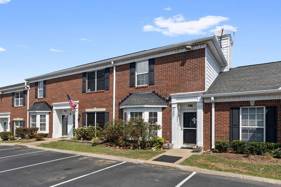 Front view of a two-story brick townhouse with white trim and parking area.