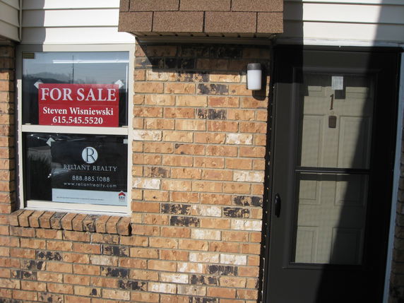 Front view of a brick building with a door and window displaying a for sale sign.