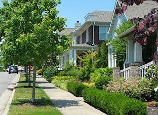 Front view of houses in a residential neighborhood with trees and a sidewalk.