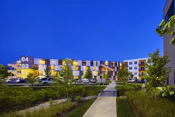 Front view of a modern multi-story apartment building with numbered floors and illuminated balconies.