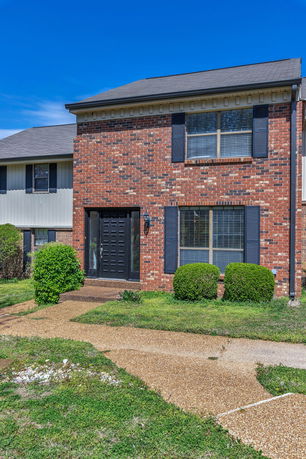 Front view of a brick house with a black door and shutters.