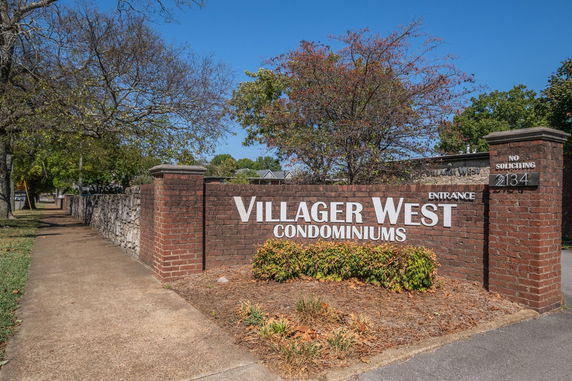 Front view of a condominium entrance with a brick wall and sign.