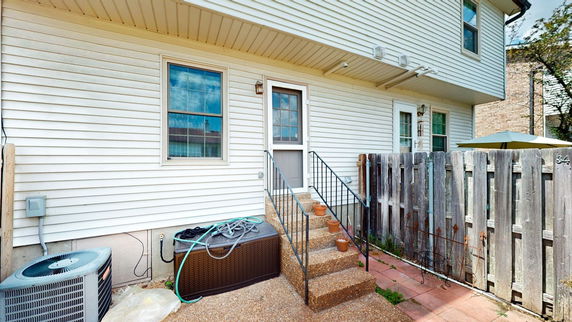 Back view of a house with steps leading to a door and a wooden fence nearby.