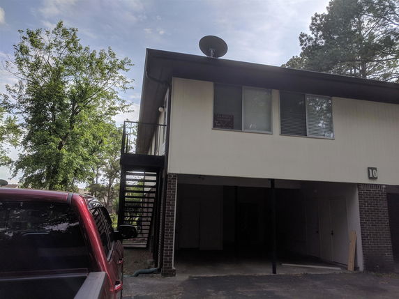Front view of a two-story building with an external staircase and partially covered parking area.