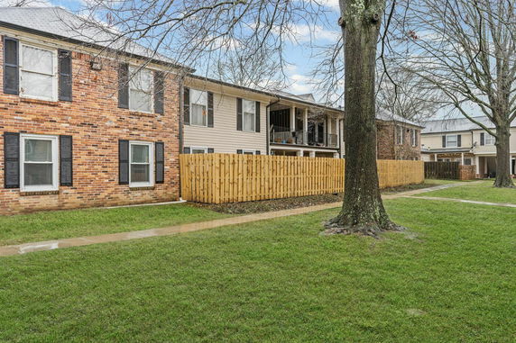 Front view of a two-story building with brick and siding walls, featuring multiple windows and a wooden fence.