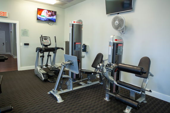 Indoor gym area with exercise equipment including an elliptical and leg extension machines.