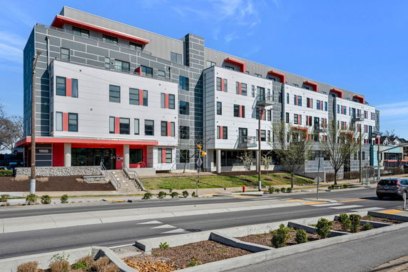 Front view of a modern, multi-story building with red accents and large windows.