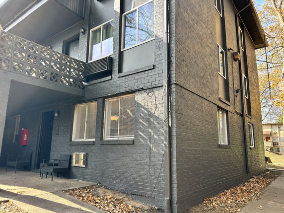 Front view of a multi-story apartment building with an exterior stairway and outdoor seating.