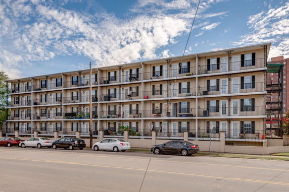Front view of a four-story apartment building with balconies and parking area.
