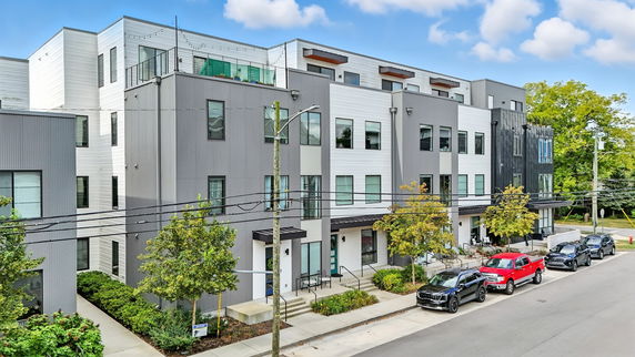 Front view of a modern multi-story building with balconies and parked cars.