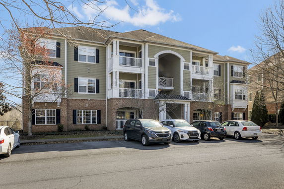 Front view of a three-story apartment building with multiple balconies and a parking area.