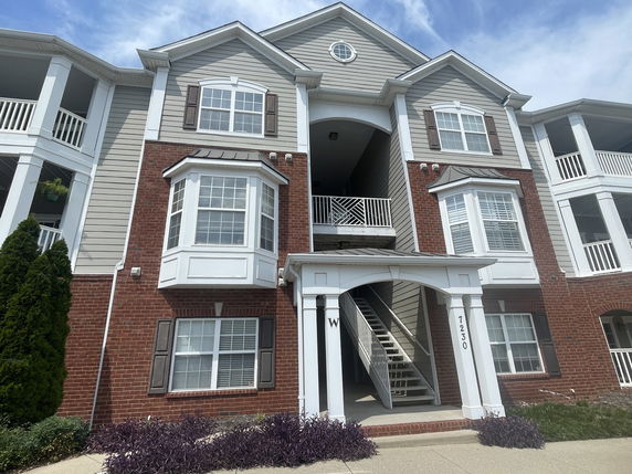 Front view of a multi-story apartment building with brick and siding exterior and a central stairway entrance.