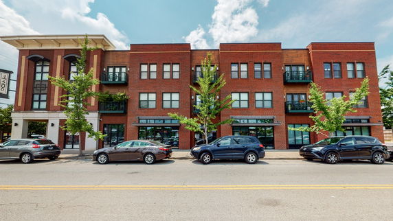 Front view of a three-story brick apartment building with balconies and street parking.