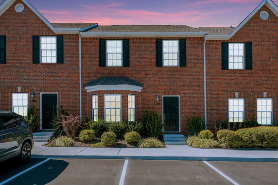 Front view of a two-story brick townhouse with black shutters and a bay window.