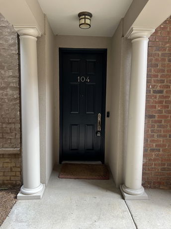 Front entrance of a building with a black door numbered 104 and white columns.