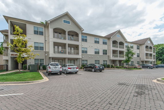 Front view of a multi-story apartment building with balconies and a parking area.